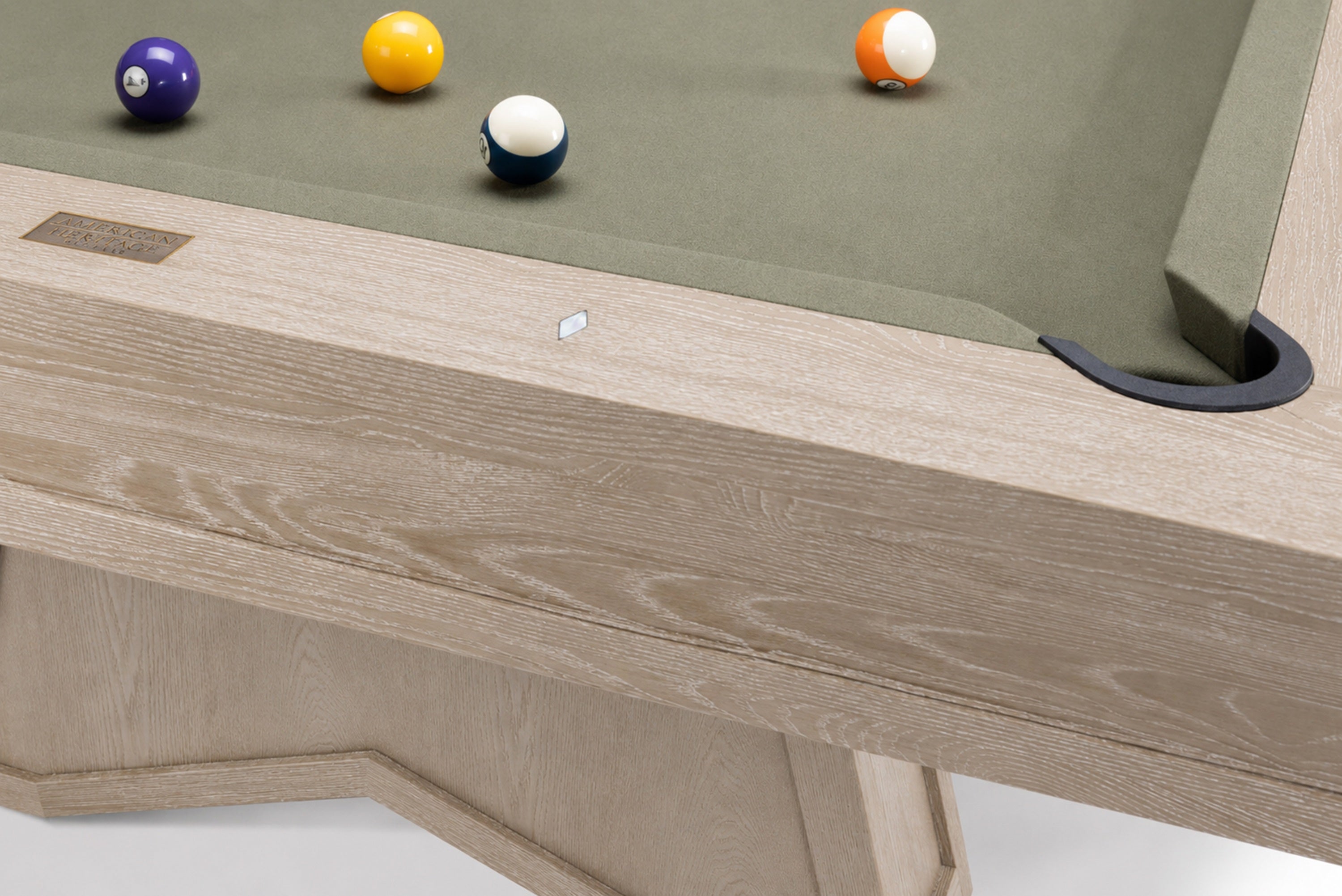 Close-up of a wooden pool table showing the light oak frame, green felt surface, and several billiard balls on a white background.