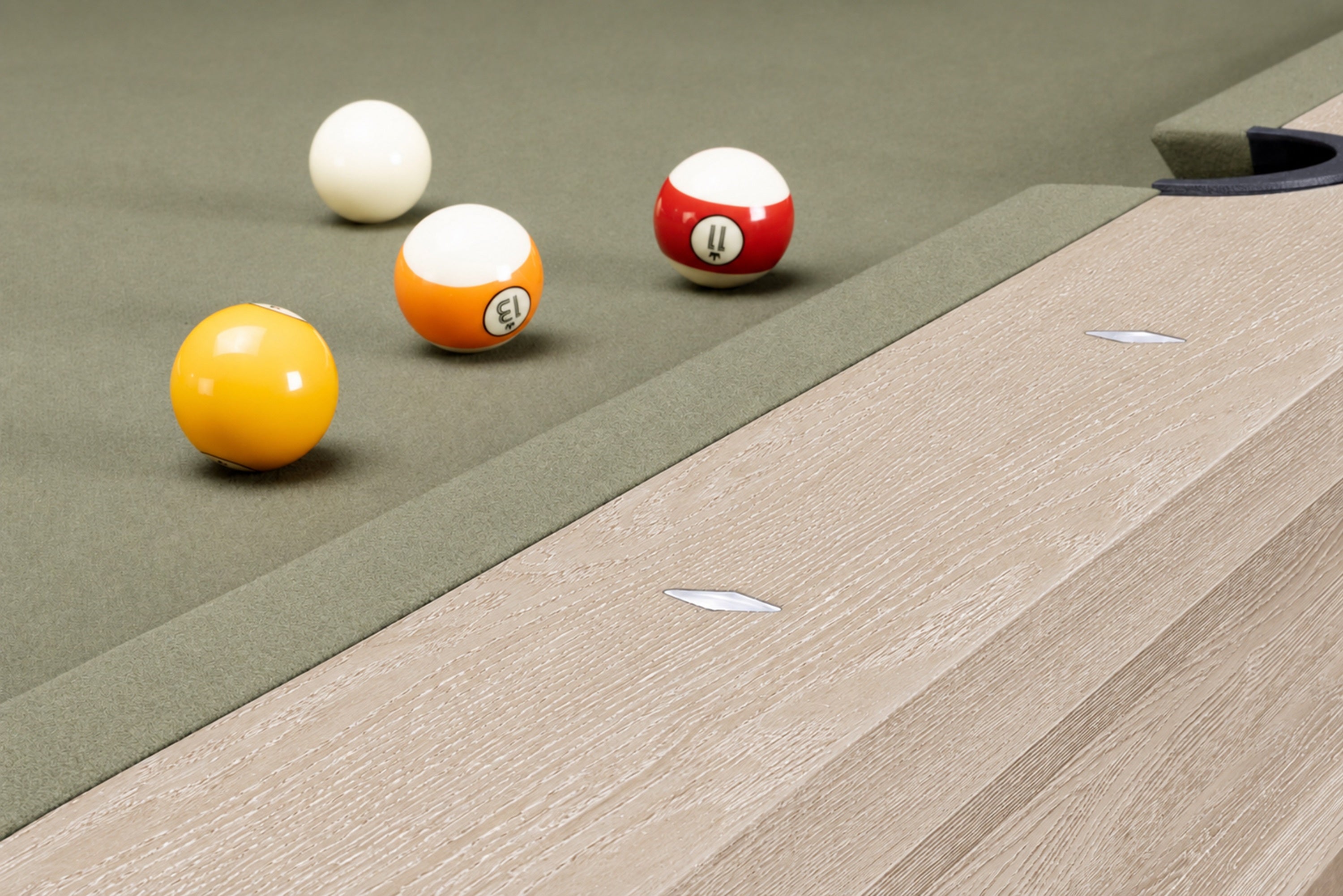 Close-up of a pool table corner with four billiard balls on a green felt surface and a light wood grain rail.