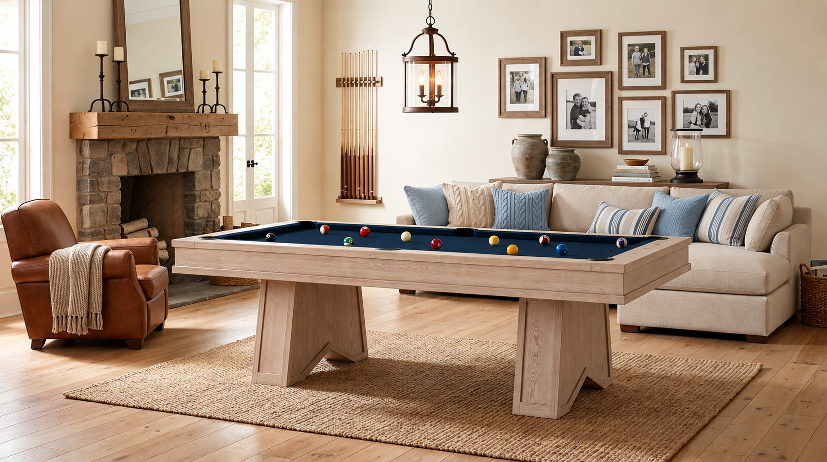 A light natural wood pool table with a blue felt playing surface and colorful billiard balls, set in a beautifully styled living room with a fireplace, sofa, and framed wall art.