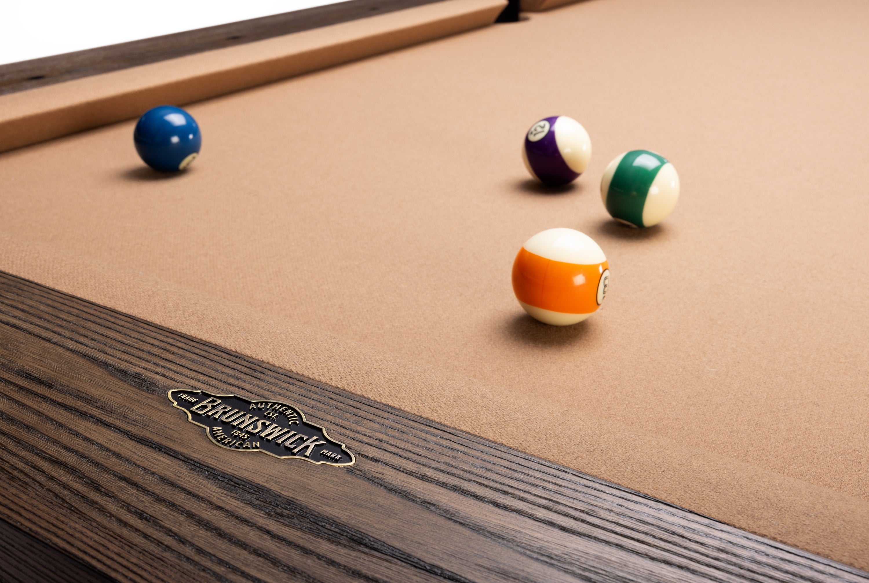 Close-up of a BenNSWIK pool table with a tan felt surface and dark wood frame, showing several billiard balls on the table.
