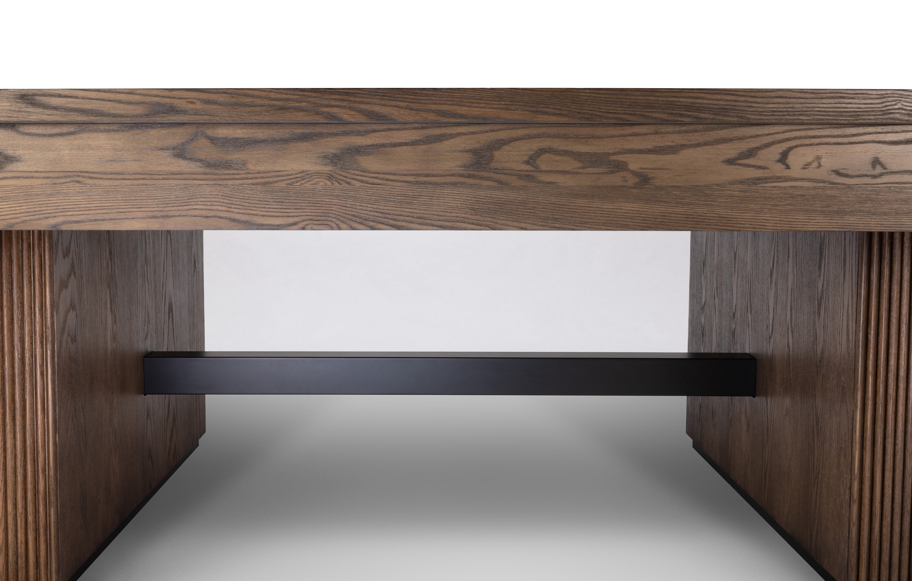 Close-up of a modern wooden table or console table showing the thick wood grain top, fluted side supports, and a black metal shelf rail underneath, photographed against a clean white studio background.